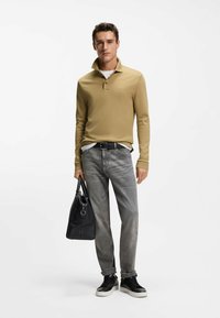 Beżowa polo z długim rękawem, kołnierzykiem i logo, w zestawie z szarymi dżinsami, czarnymi trampkami i czarną teksturowaną torbą na ramię.