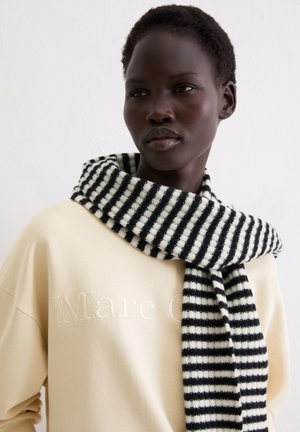 Czarnobiały prążkowany dziergany szalik zarzucony na szyję, zestawiony z kremową bluzą z wypukłym logo.