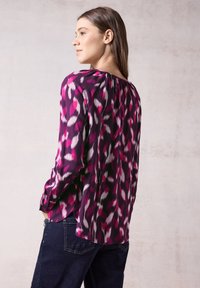 Blusa a maniche lunghe in un vivace motivo astratto nei toni del viola, rosa e bianco. Presenta un colletto arricciato e una texture liscia e leggera.