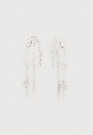 Brincos em tom prateado com pedras transparentes em formato de marquise e gota, e finesse de correntes penduradas em comprimentos variados sobre um fundo branco.