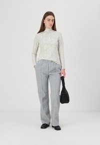 Light gray floral print turtleneck sweater, paired with high-waisted gray trousers and a textured black handbag. Smooth fabric finish.