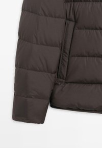 Giubbotto imbottito marrone scuro con sezioni cucite, texture liscia, tasca laterale e una vestibilità leggermente oversize. Realizzato in materiale leggero e isolante.