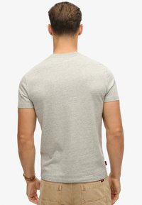 Maglietta grigia a maniche corte con colletto rotondo, realizzata in tessuto misto cotone, con una leggera texture e una piccola etichetta rossa sul fondo.
