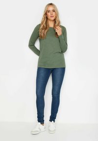 Olivgrön långärmad topp i kombination med blå skinny jeans och vita sneakers; avslappnad passform, mjuk textur och enkel design.