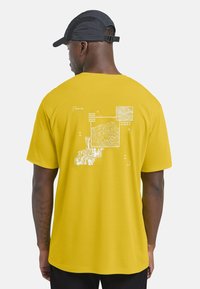 T-shirt gialla a maniche corte con design grafici bianchi sulla schiena, inclusi mappe e coordinate, con una vestibilità rilassata.
