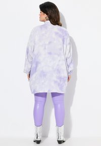 Maglietta a maniche lunghe, di colore viola con effetto tie-dye, dal taglio rilassato, abbinata a leggings lavanda lucidi e stivaletti argentati. Trame morbide e colori vivaci.