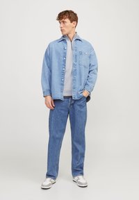 Chemise en denim bleu clair avec une poche poitrine superposée à un sweat gris, associée à un jean bleu et des baskets grises. Coupe décontractée.
