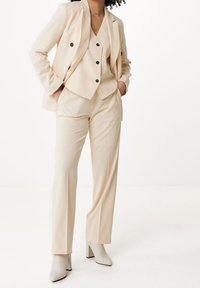 Bledě béžový oblek s přiléhavým blejzrem s černými knoflíky, odpovídajícími kalhotami a světle šedými kozačkami na podpatku do výšky kolen. Hladká textura.