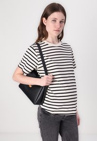 Geantă de piele neagră cu un design structurat, având un accent bej. Purtați-o cu un tricou striped în negru și crem și blugi gri.