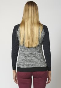 Strickpullover mit einem grau gemusterten Körper und dunklen Ärmeln, versehen mit einem schwarzen gerippten Saum und strukturiertem Stoff für zusätzlichen Interessantes.