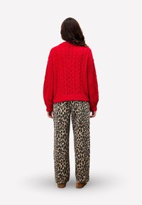 Un pull en maille rouge avec des manches larges associé à un pantalon léopard ample, mettant en valeur un motif texturé et des teintes neutres.