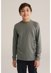 Hosszú ujjú, olívazöld póló, puha anyagból, kerek nyakkal, amelyen egy függőleges sötétkék "SALT DOG" grafika található az oldalon.