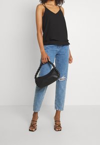 Black sleeveless top with a layered hem, paired with blue distressed jeans. The model holds a black braided handbag and wears black strappy sandals.