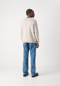 Lysegrå sweatshirt med ribbede manchetter og kant, parret med blå denim jeans. Jeansene har et klassisk fem-lomme design.