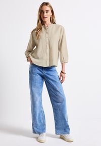 Ljusbeige skjorta med mandarinkrage och trekvartsärmar, ihop med vida ljusblå denimjeans.