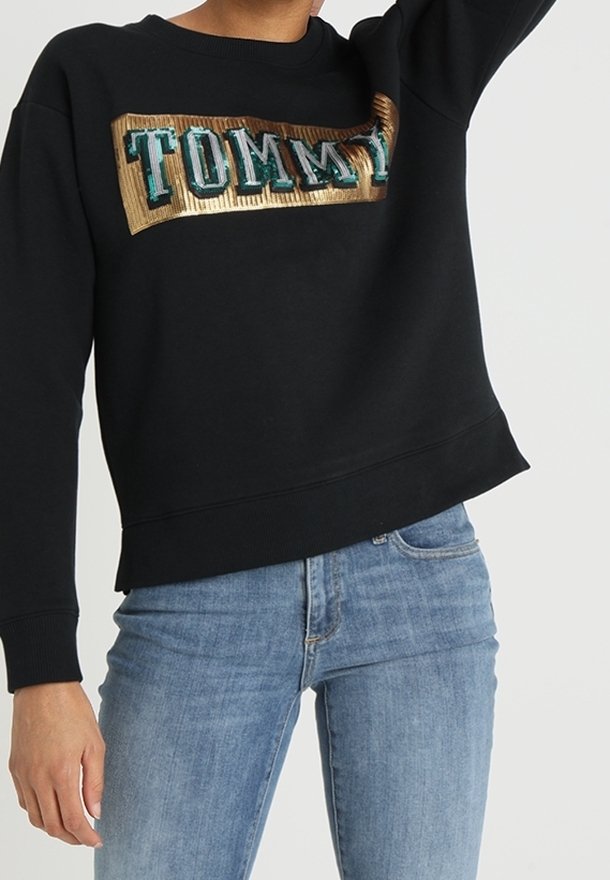 Czarna bluza z fakturą prążkowaną, z dużym logo "TOMMY" w kolorach morskim i złotym na przodzie. Casualowy design, luźny krój.