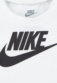 Bela bomba majica iz bombaža z velikim črnim logotipom Nike in odtisom v drznem tisku čez prsni del. Mehka tekstura.
