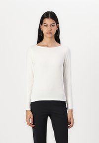 White long-sleeve sweater in soft texture with a boat neckline, featuring slim fit and side slits, paired with black trousers.