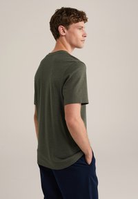 Camiseta de algodón color verde oliva con cuello redondo, mangas cortas y un corte relajado. Textura suave y dobladillo curvado en la parte posterior.