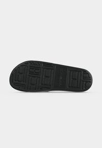 Semelle de chaussure noire avec des motifs rectangulaires et carrés texturés et "Tommy Hilfiger" embossé au centre.