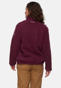 Giacca in fleece bordeaux con collo alto, caratterizzata da un logo sulla schiena e maniche lunghe. La texture è morbida e spessa.