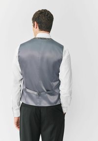 Szary satynowy kamizelka o gładkiej fakturze, z tylnym paskiem i ozdobnym wzorem wzdłuż kołnierza, w komplecie z białą koszulą z guzikami.