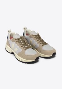 Beige and gray mesh sneakers with suede accents, oval toe, round laces, and a white midsole. Rear features a dark blue tab.