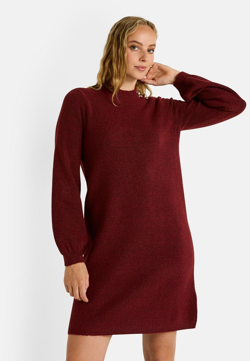 Vestido de punto burdeos con mangas largas, cuello redondo y puños acanalados. Presenta una textura sutil y un corte ligeramente holgado.