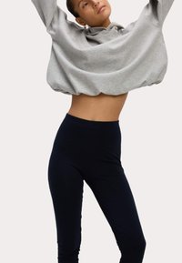 Grijze hoodie met een losse pasvorm, gecombineerd met hoge zwarte leggings. De stof lijkt zacht en soepel met minimale details.