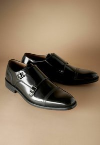 Zwarte leren schoenen met een glanzende afwerking, voorzien van dubbele gespen, een geprofileerd paneel en een spitse neus. Glad zool met subtiele stiksels.