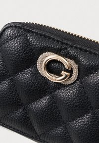 Čierna prešívaná kožená peňaženka s zlatým logom na zapínaní, ozdobená jasnými rhinestonmi. Zipsové uzatvorenie s textúrovaným povrchom.