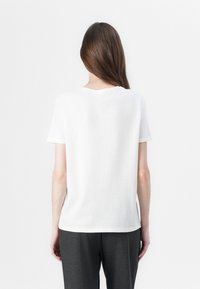 White cotton t-shirt with short sleeves and a round neck, featuring a relaxed fit and straight hem, paired with dark gray pants.
