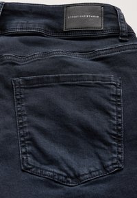 Jeans de mezclilla de un azul oscuro con una etiqueta de cuero que dice "STREET ONE STUDIO", con costuras visibles y un bolsillo trasero.