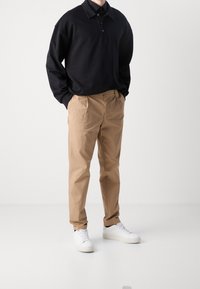 Černé polo tričko s dlouhým rukávem, béžové chinos kalhoty, bílé tenisky. Polo má límec a knoflíky; chinos jsou rovné, z hladké látky.