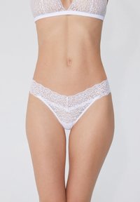 Weißes Spitzentop und passender Tanga mit floralem Muster, weicher Textur und gewellten Kanten. Dehnbare Bänder für Komfort und passgenauen Sitz.