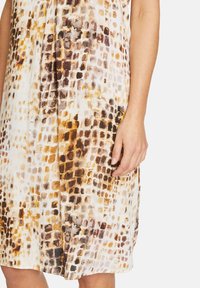 Kevyt mekko, jossa on löysä istuvuus, esittäen teksturoidun ruutukuvion ruskean ja beige sävyissä, valmistettu pehmeästä kankaasta, jossa on hienoinen kiilto.