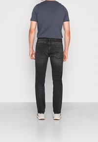 Vaqueros de mezclilla negros con un corte recto, bolsillos traseros y una textura sutilmente descolorida. Combinados con una camiseta azul oscura y zapatillas claras.