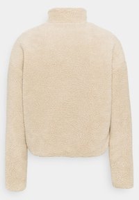 Giacca in pile beige, strutturata, con colletto alto e maniche lunghe. Presenta un design corto e una superficie morbida e pelosa.