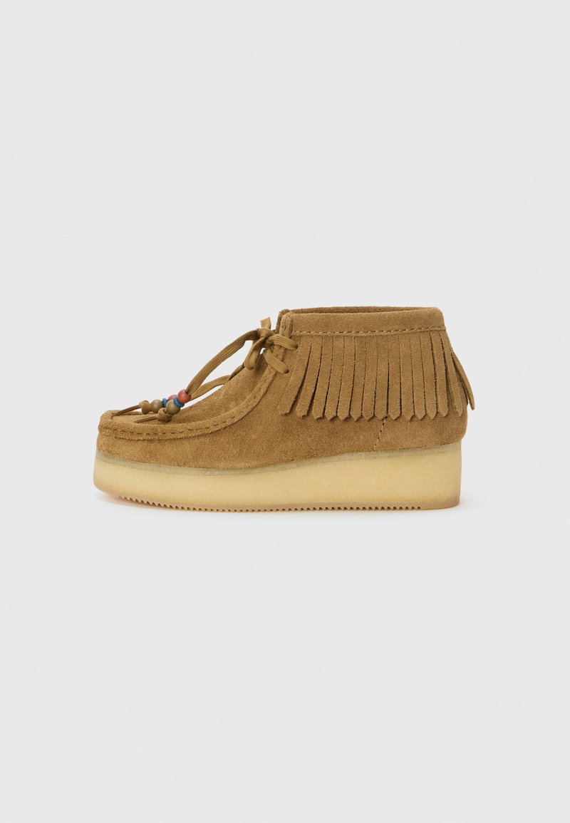 Chaussure mocassin en cuir suédé marron avec des détails en franges, bout arrondi, accents décoratifs en perles et une semelle plate-forme en caoutchouc de couleur claire.