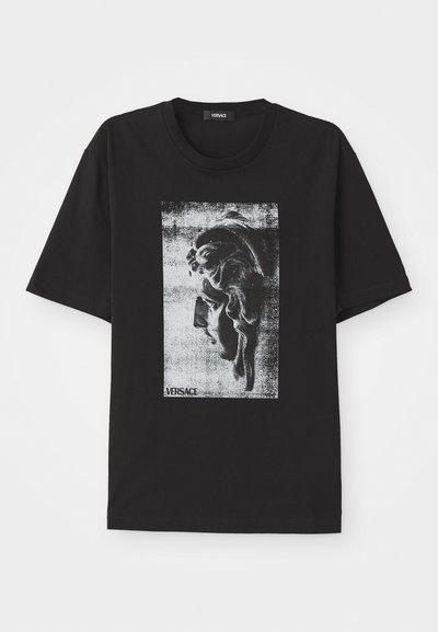 T-shirt noir en coton avec un imprimé graphique d'un visage classique en niveaux de gris. Col rond et manches courtes. Logo Versace présent.