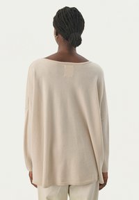 Beiger, übergroßer Pullover mit weitem Ausschnitt, überschnittenen Schultern und geripptem Saum. Glatte Textur und minimale Details auf der Rückseite.