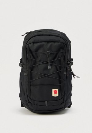 Zwarte Fjällräven-rugzak met elastisch koord aan de voorkant, zijvakken, meerdere compartimenten en een logopatch op een effen achtergrond.