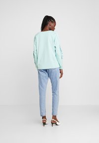 Sweatshirt azul claro com um corte descontraído e mangas franzidas, combinado com jeans azul claro e sapatos de salto brancos.