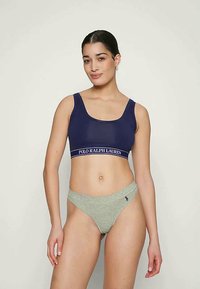 Bralette bleu marine avec bande de logo blanche ; associé à un thong gris clair arborant un petit logo. Tissu lisse et design sans coutures.