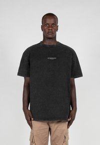 Sort kortærmet T-shirt i en falmet vask med en rund halsudskæring. Har et lille hvidt tekstlogo på forsiden. Lavet af bomuldsstof.
