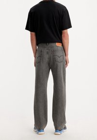 Svart t-shirt, grå vida jeans i texturerad tyg, bakpatch-märke och två bakfickor. Skorna har kontrasterande blå accenter.