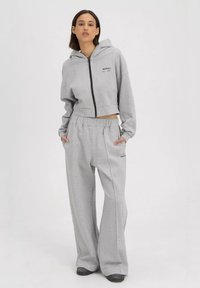 Grijze cropped hoodie met rits en zakken, gecombineerd met brede grijze sweatpants met een elastische tailleband en merkembleem. Zachte, gestructureerde stof.