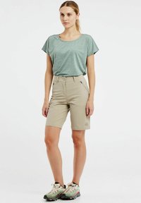 Svetlozelený krátky rukáv top; pieskové kraťasy s dvoma prednými vreckami; oboje vyrobené z ľahkého materiálu. Nosí sa s šedými turistickými topánkami.