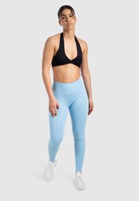 Czarny halter top sportowy zestawiony z jasnoniebieskimi legginsami z wysokim stanem i białymi butami sportowymi. Gładki materiał z dopasowanym krojem.