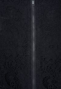 Černá krajková látka s květinovým vzorem a viditelným zipem uprostřed. Materiál vypadá jemně s propracovanými detaily a texturou.